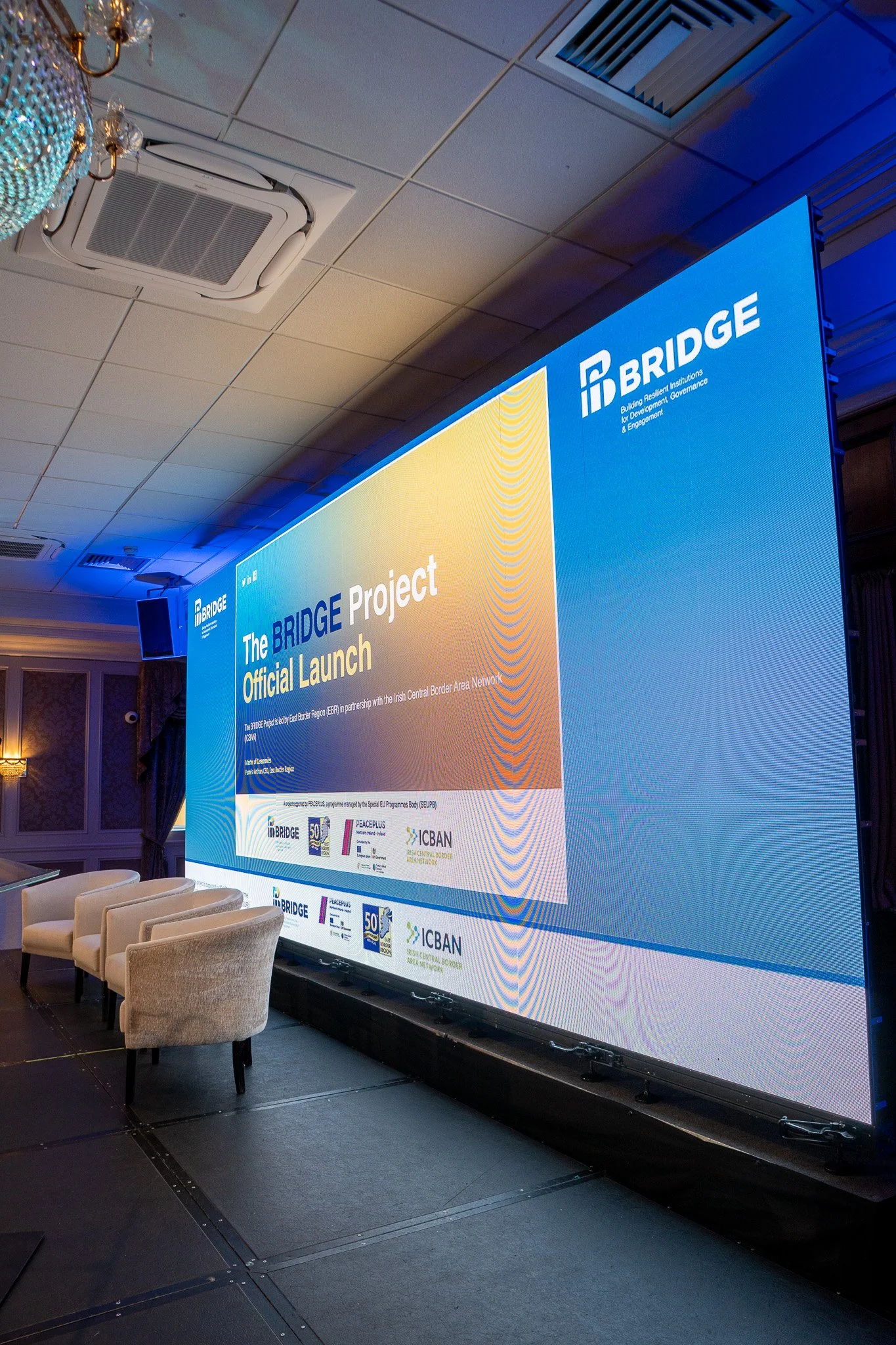 BRIDGE Project Official Launch title on a 2.9mm LED video wall, four armchairs set on stage for the panel at Canal Court Hotel.