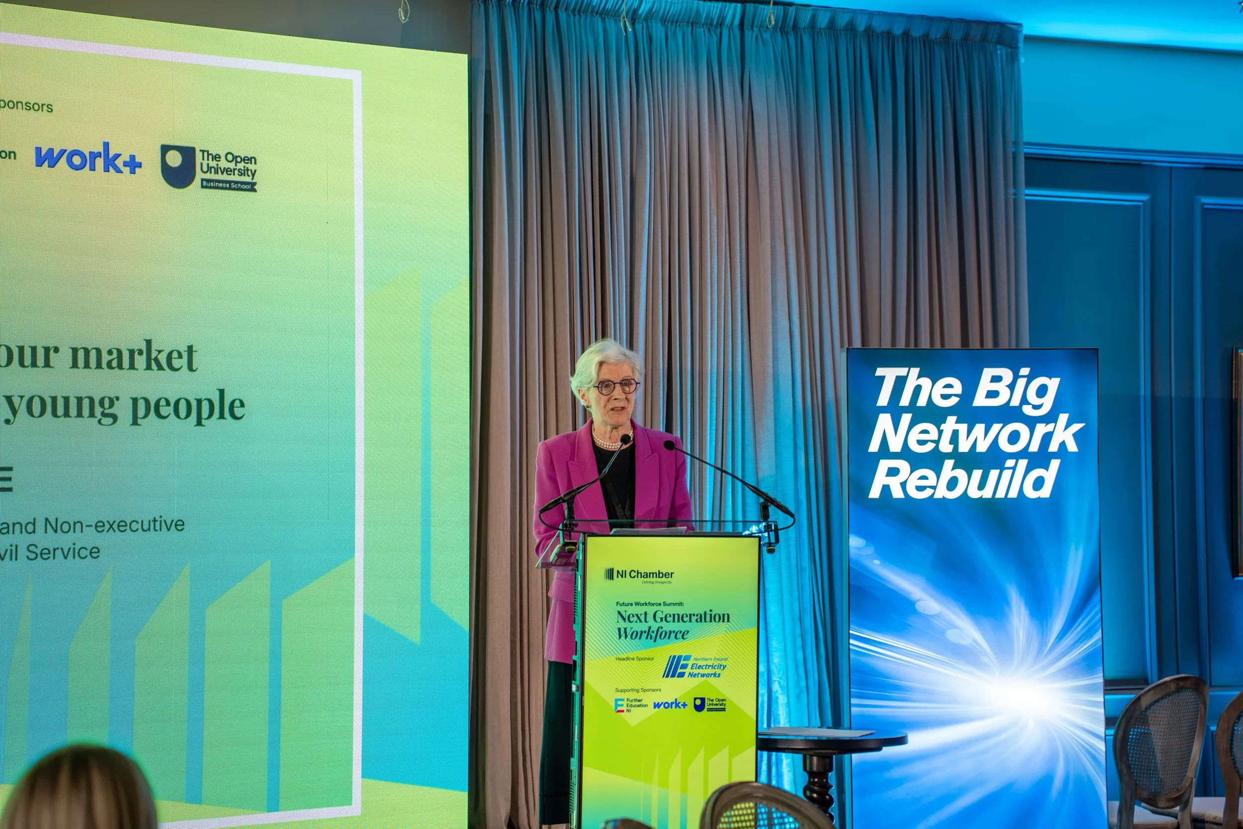 Keynote speaker at a branded digital lectern beside an LED wall title slide on building a labour market for young people