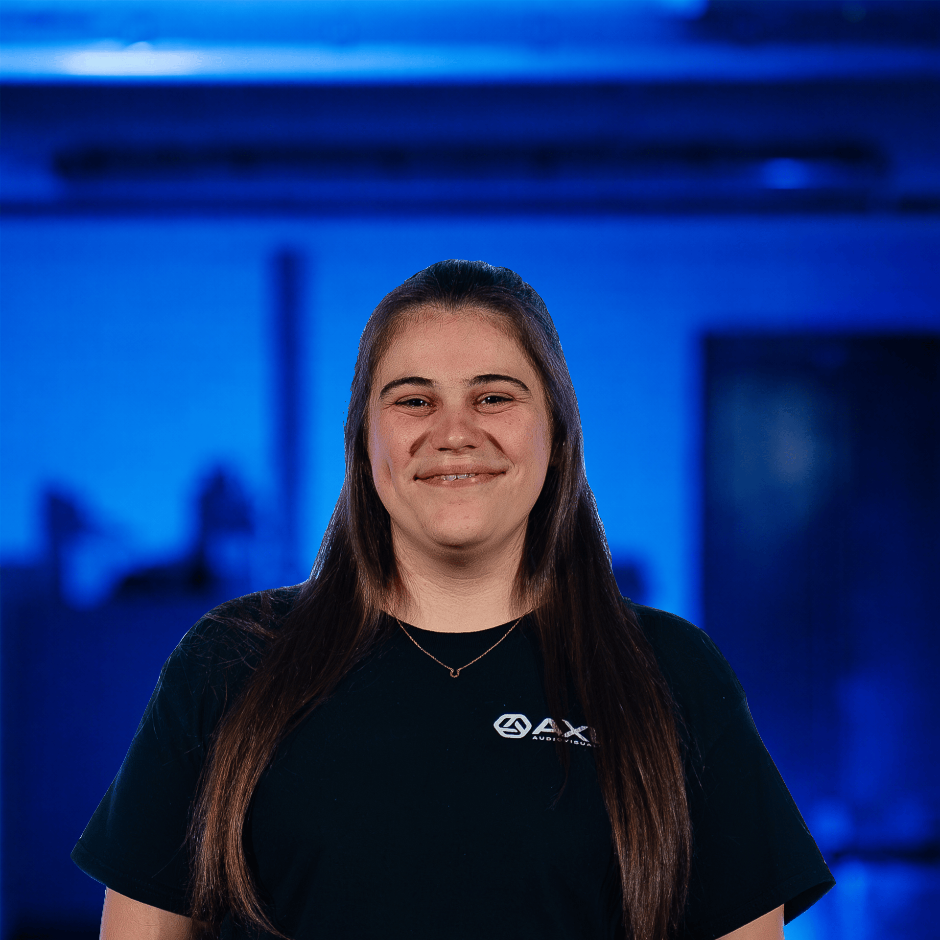 A smiling woman standing on a stage with colorful lights and a large screen in the background. 