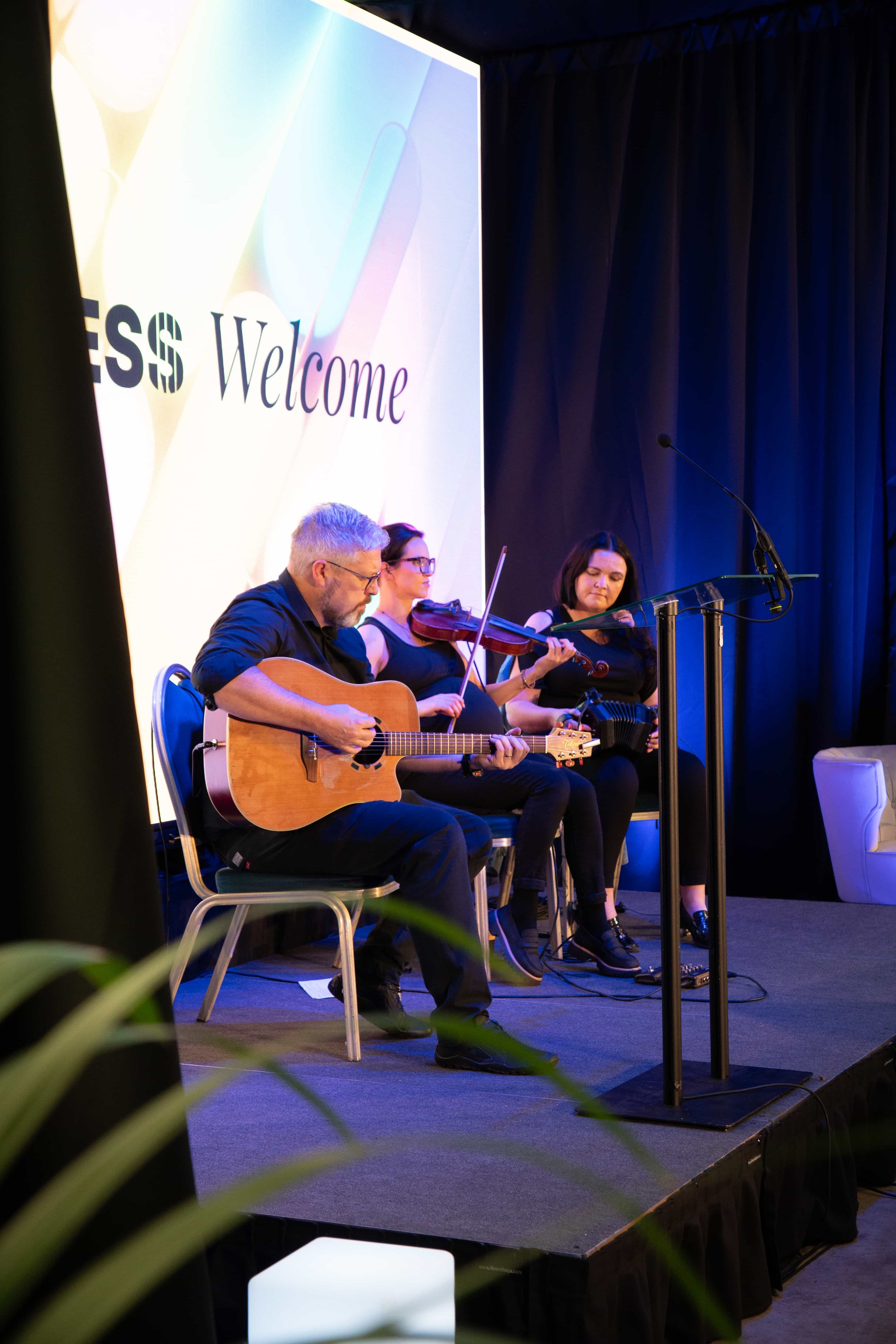 Traditional Irish music trio playing guitar, fiddle and concertina on the main stage before the conference opened