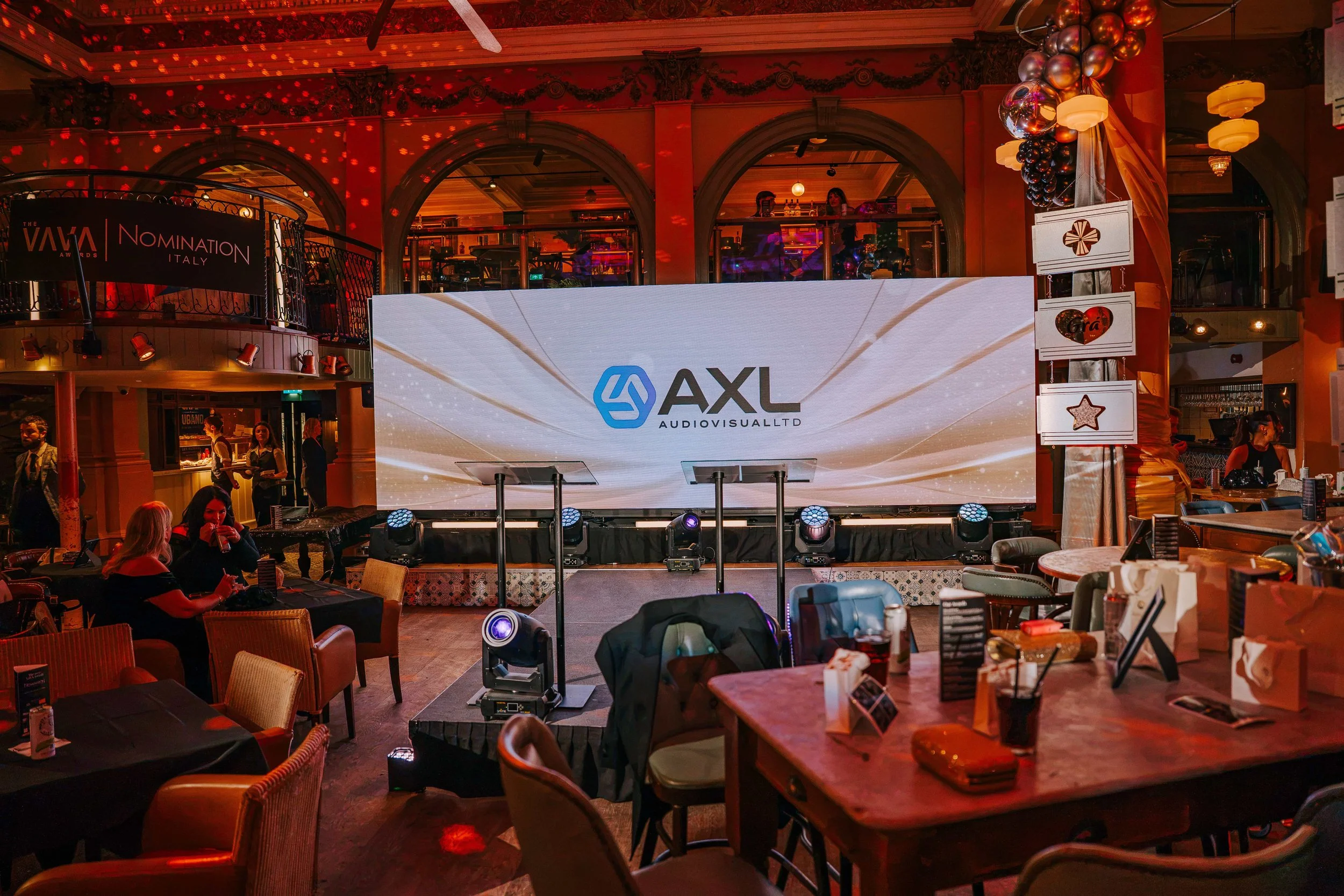 AXL Audiovisual logo on a 2.9mm LED wall above a stage with two glass lecterns and a row of moving head lights at the VAVA Awards 2026