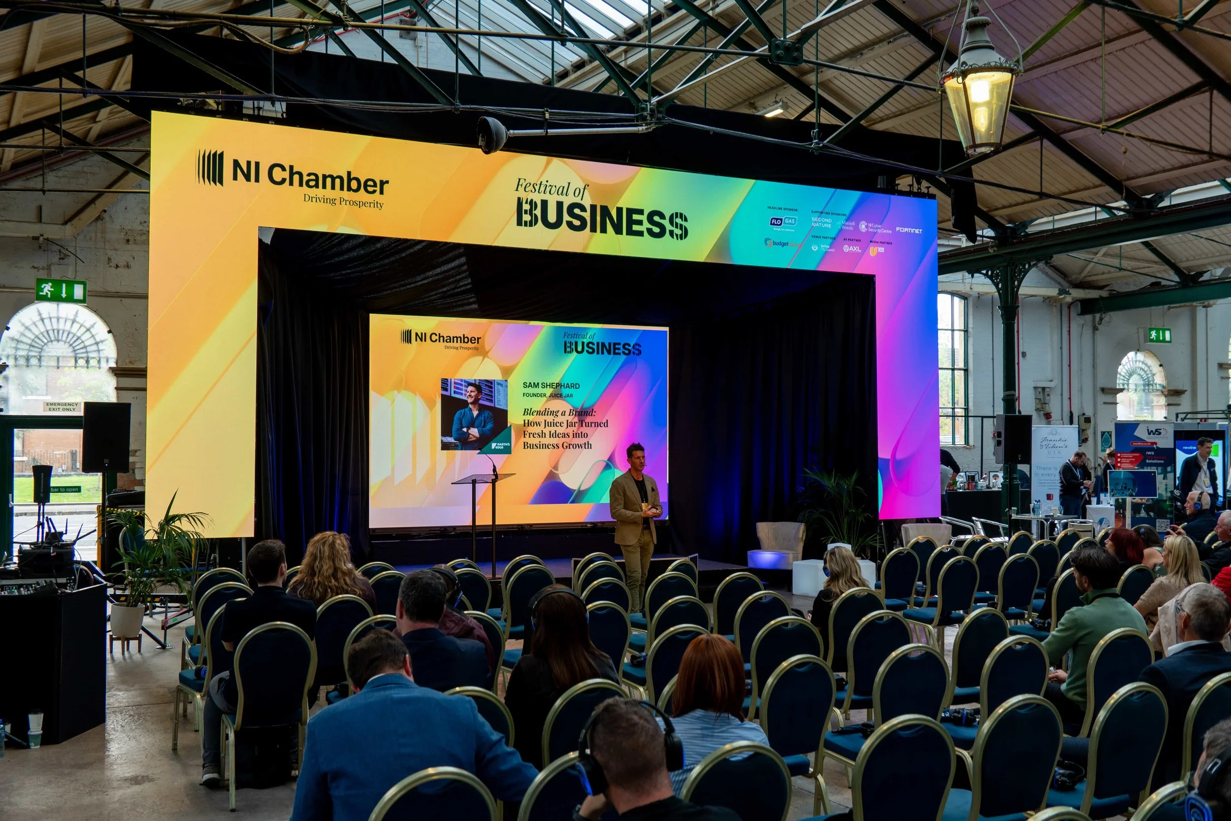Sam Shephard presenting with a headset microphone in front of the main stage LED video wall