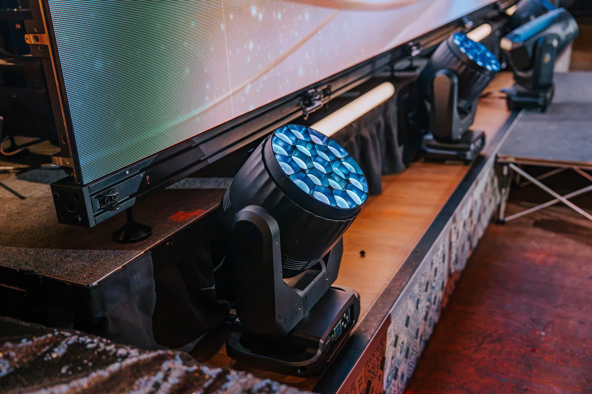 Close-up of an LED beam wash moving head on the stage riser beneath the LED video wall