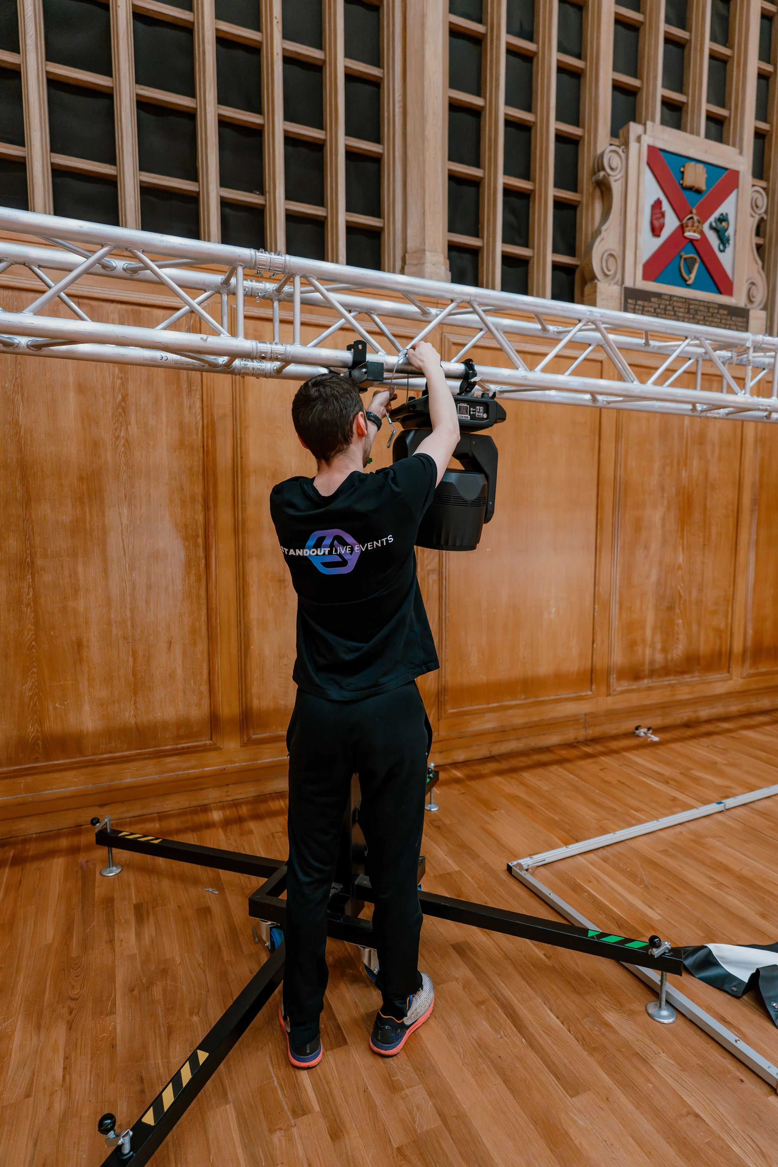 AXL technician raising ground-support truss on a lifting tower in a wood-panelled event hall