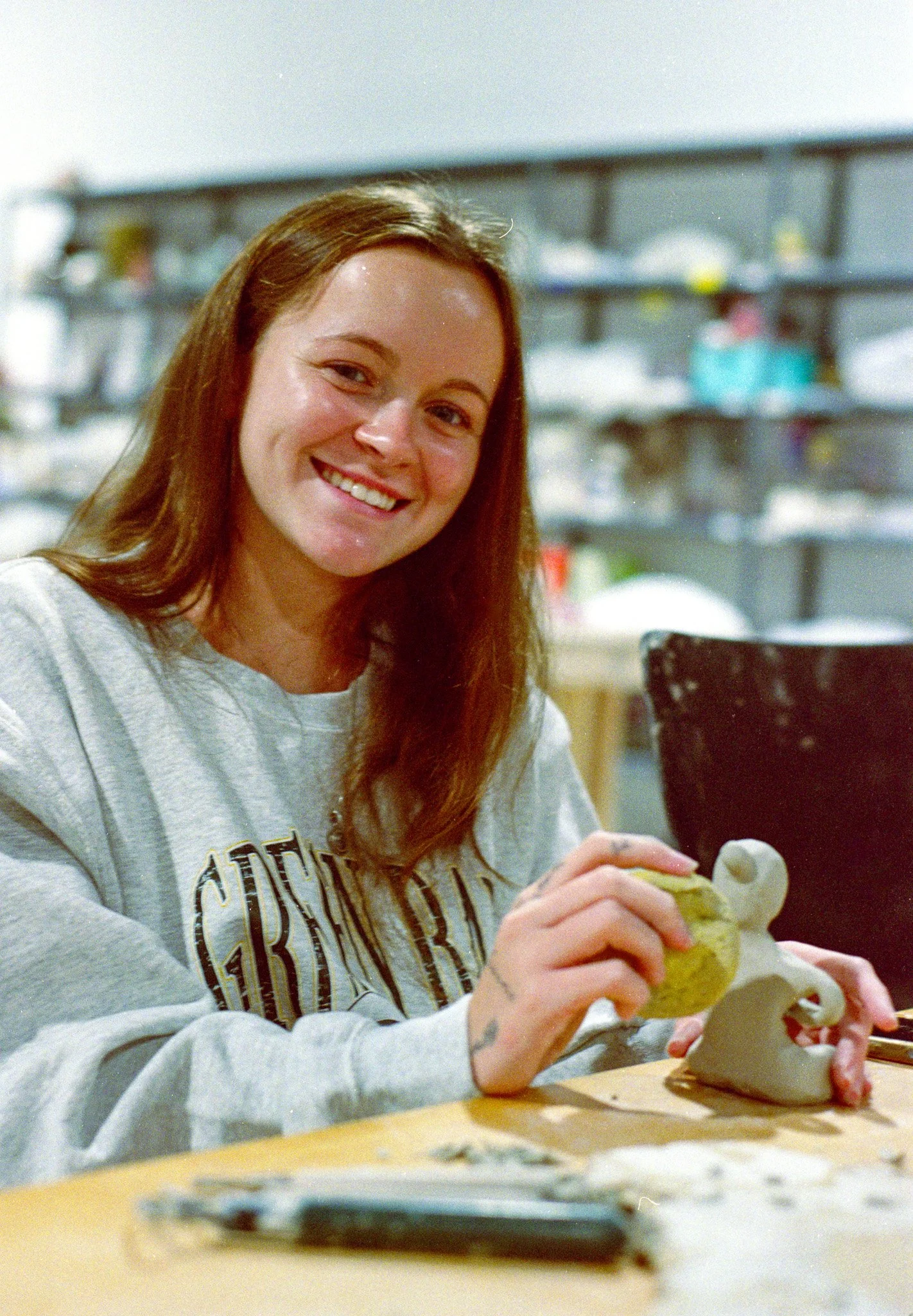 Young woman smiling, using a spong to smooth the surface of a sculpted figurine made out of clay