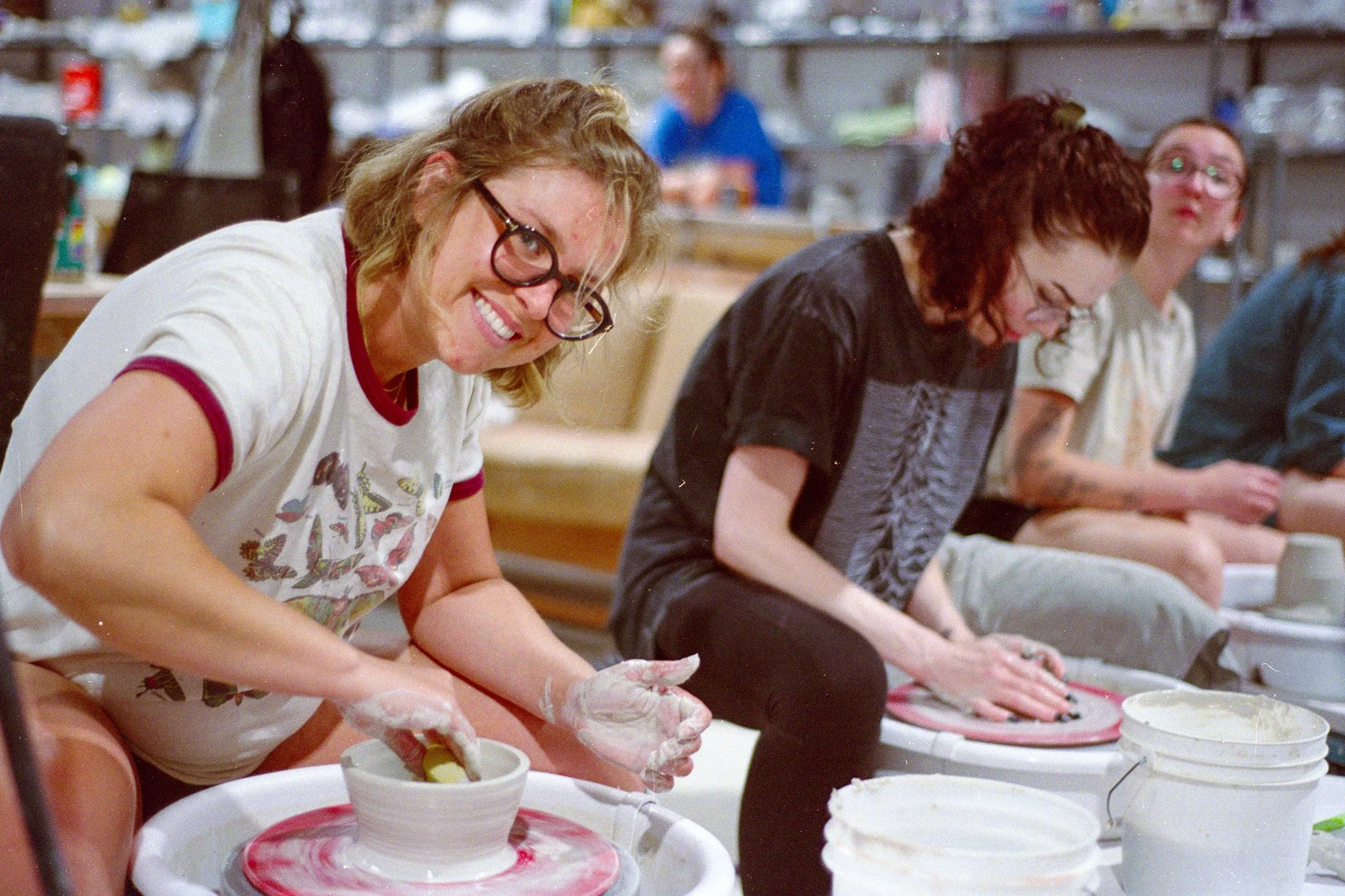 A woman wearing glasses uses a spong to shape the inside of a bowl on a pottery wheel