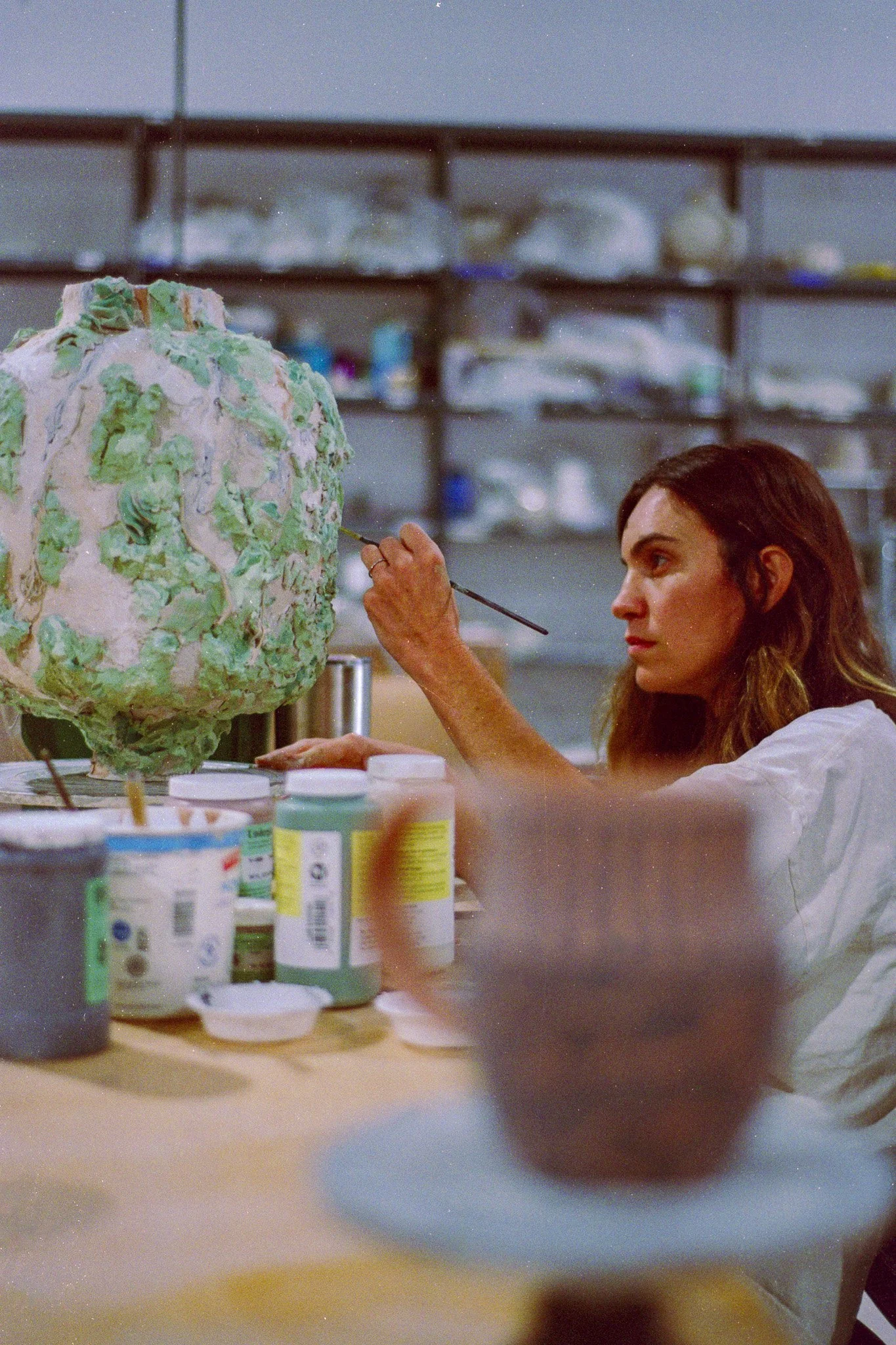 A young woman uses a brush to finely deail a large sculpture with various color glazes