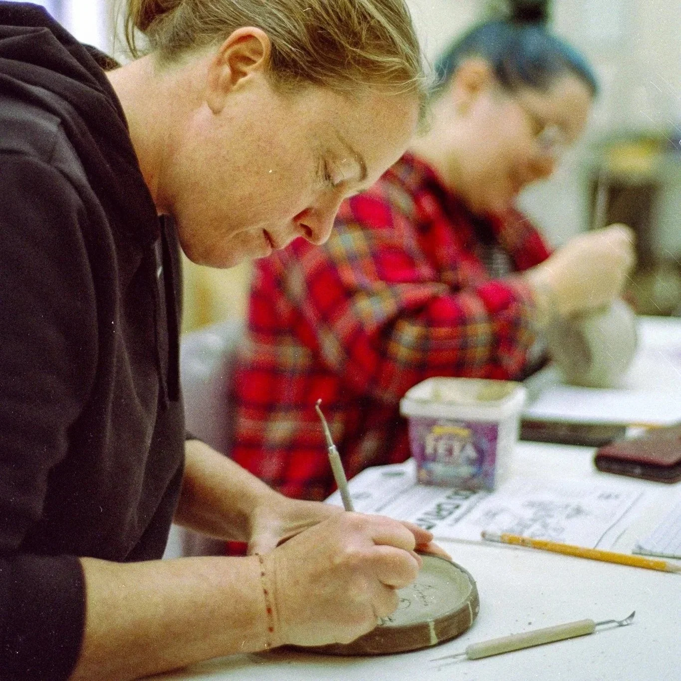 Woman works on carving a ceramic plate using a carving tool