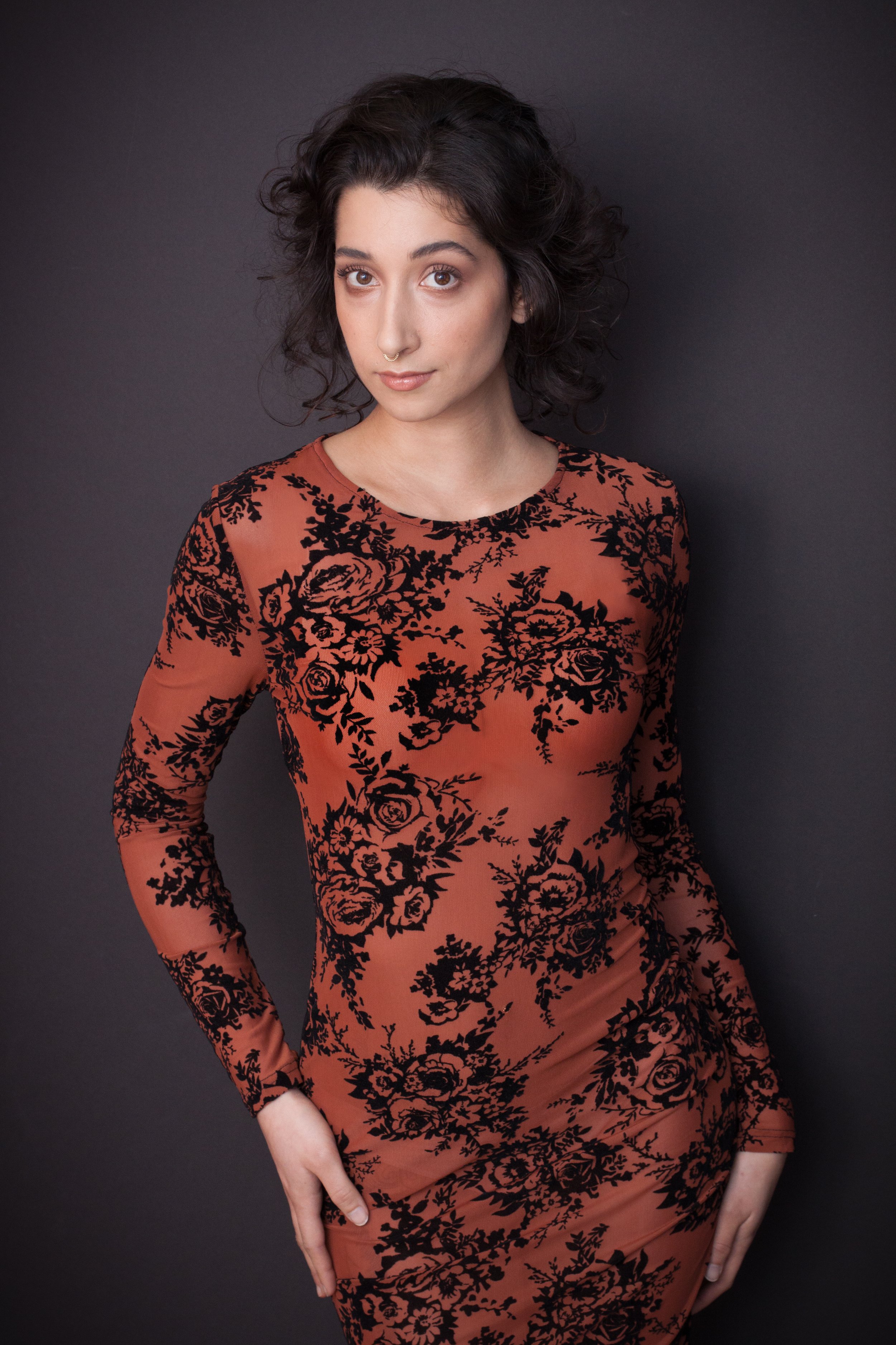 Person posing in black and orange floral dress against a gray background.
