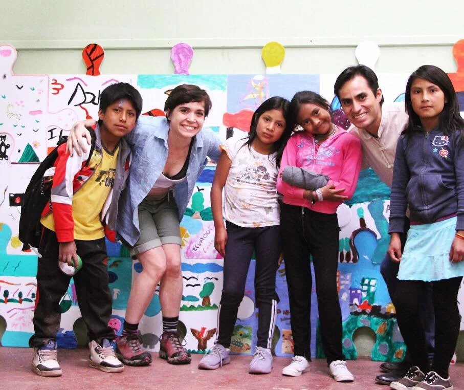 Group of children and adults posing in front of colorful wall art.