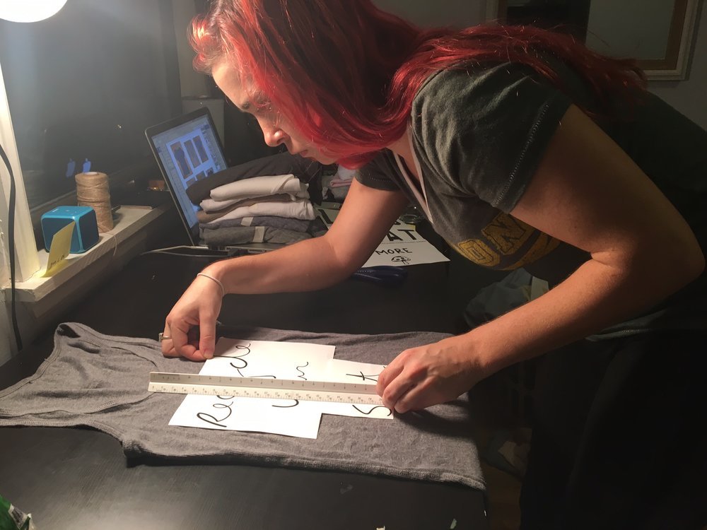 Person measuring designs on a gray T-shirt with a ruler on a desk.
