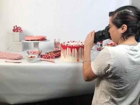 Person photographing a dessert setup with cakes and sweets on a table.