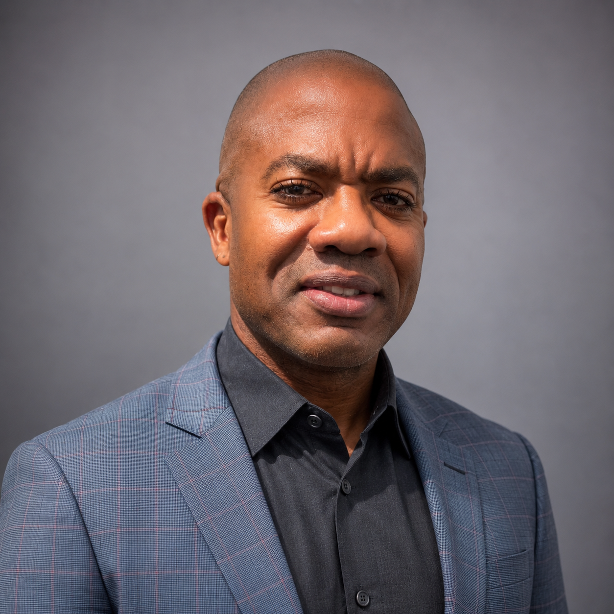 Headshot of professional Black man in grey suit and grey button-down shirt.