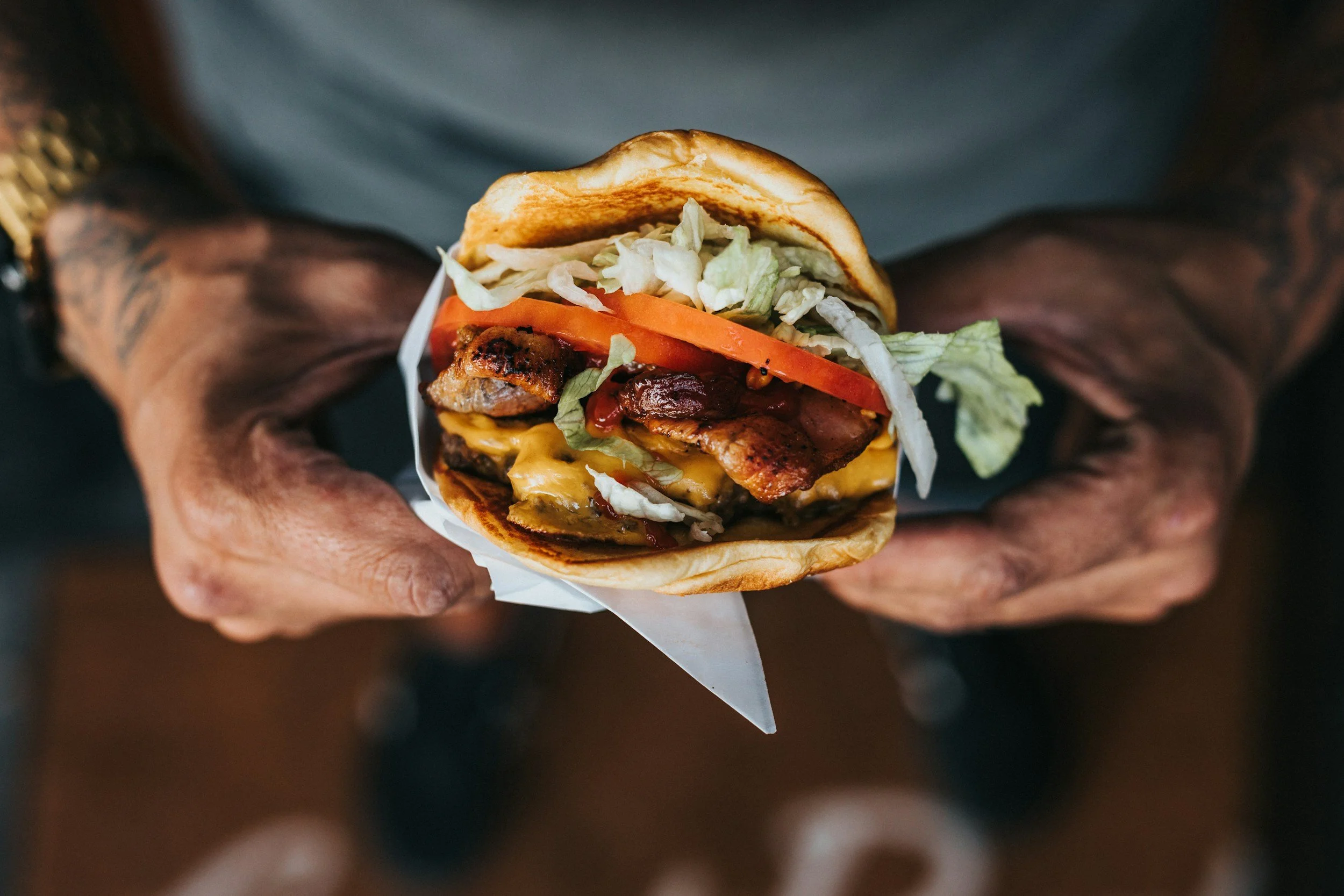 Close-up of a middle-aged man's hands holding a large burger, representing midlife binge eating and emotional eating challenges in men and women | Los Angeles San Diego San Francisco Bay Area California | 92651 90077 90266