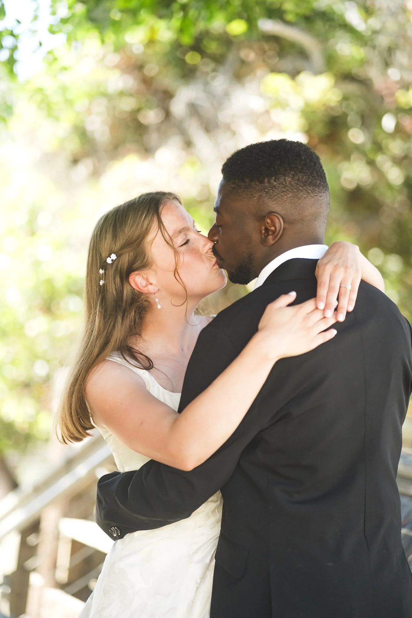 Wedding photography: bride and groom sharing kiss outdoors, bride in white dress, groom in black suit.