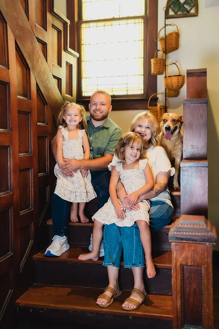 Family of four sitting together on the staircaase in their home during their lifestyle photo session.