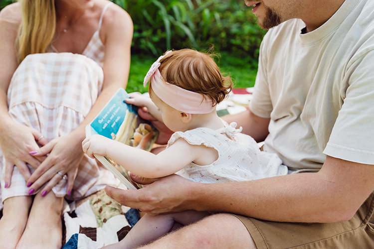 A dad reading his one-year-old daughter a story during their family portrait session.