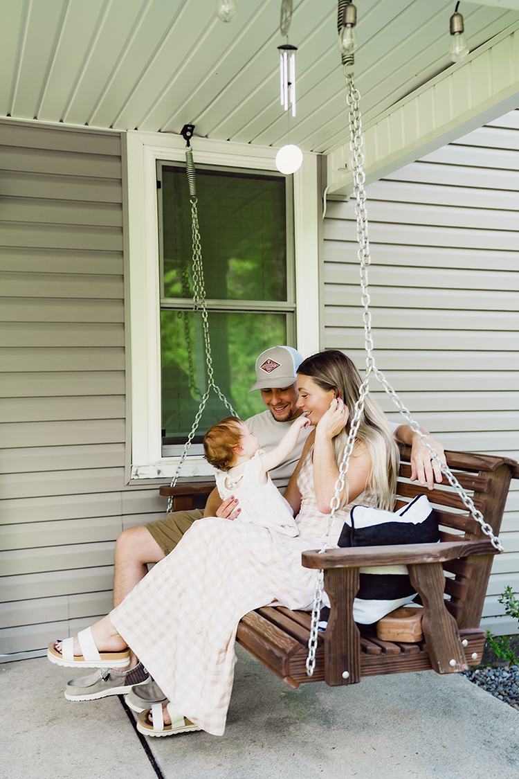 Parents and their one-year-old daughter sharing a sweet moment together on their front porch swing during a family photography session.