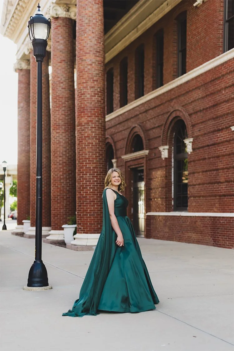 High school senior in an emerald-green prom dress standing outside a historic red brick building at night in Richmond, Indiana.