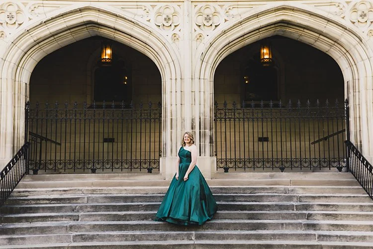 High school senior in a teal prom gown standing on the steps of a historic stone building with gothic arches and wrought-iron gates in Richmond, Indiana.