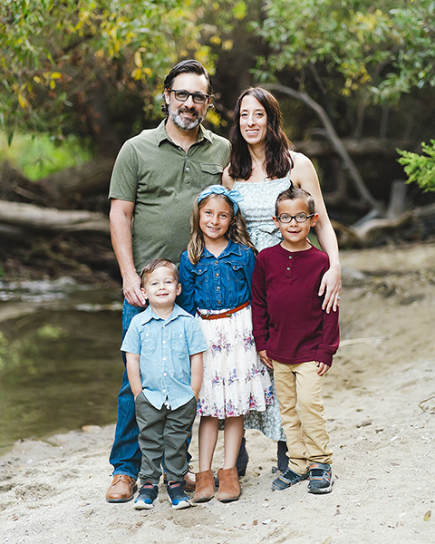 Family of five outdoors near a stream in Indiana, surrounded by green trees, standing together in a relaxed moment.