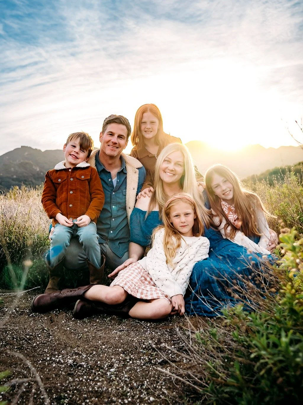 Family sitting and lying together on a hillside at sunset in Indiana with mountains and a partly cloudy sky in the background.