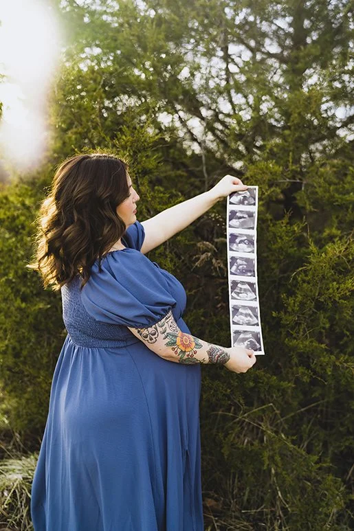 Maternity session in Indiana with pregnant woman holding ultrasound photos outdoors in natural setting.