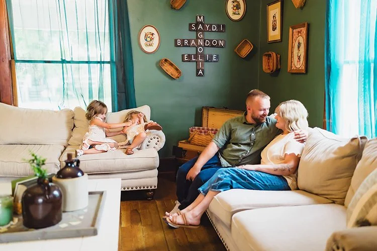 Mom and dad snuggle on the couch while the kids play beside them during an in-home family photoshoot.