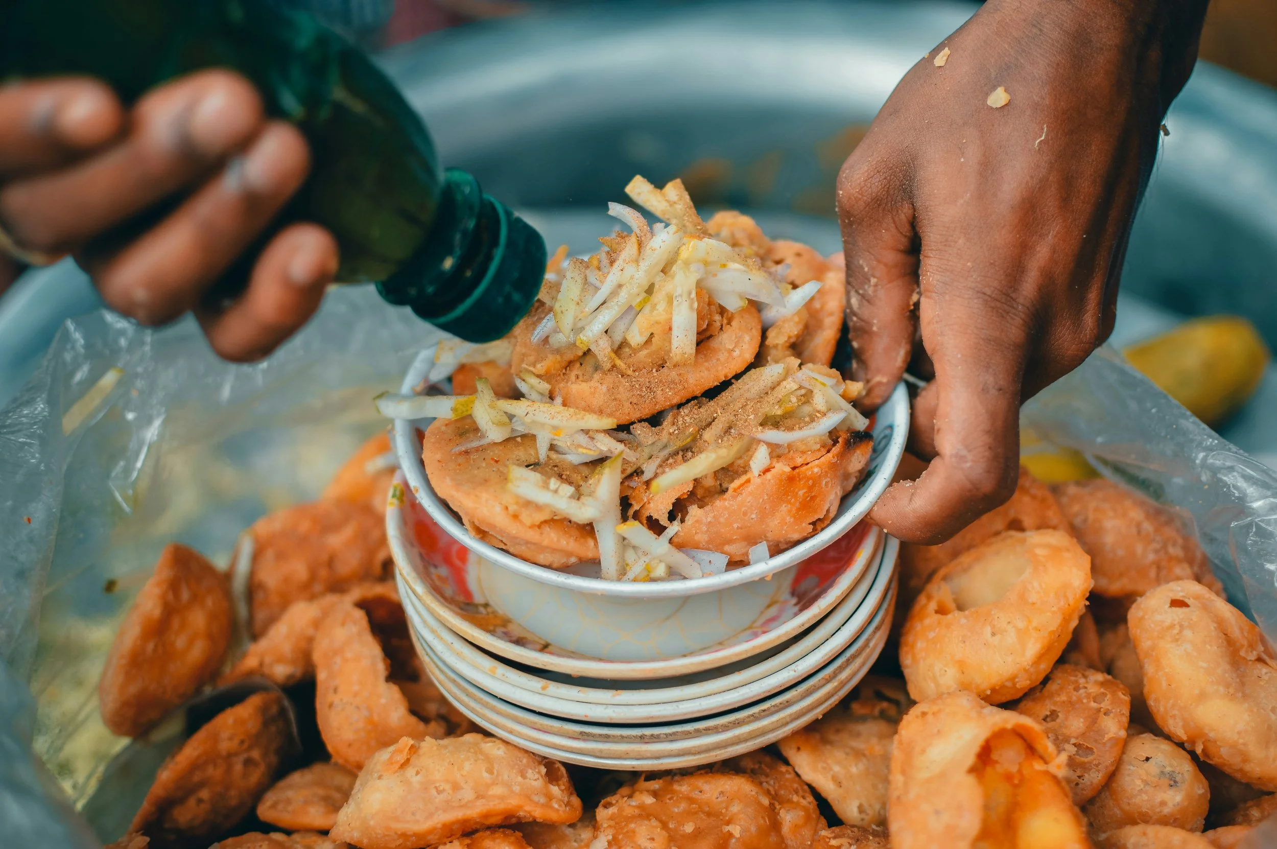 Hands stacking small bowls filled with fried fish cakes topped with shredded vegetables, with additional fried fish cakes surrounding them.