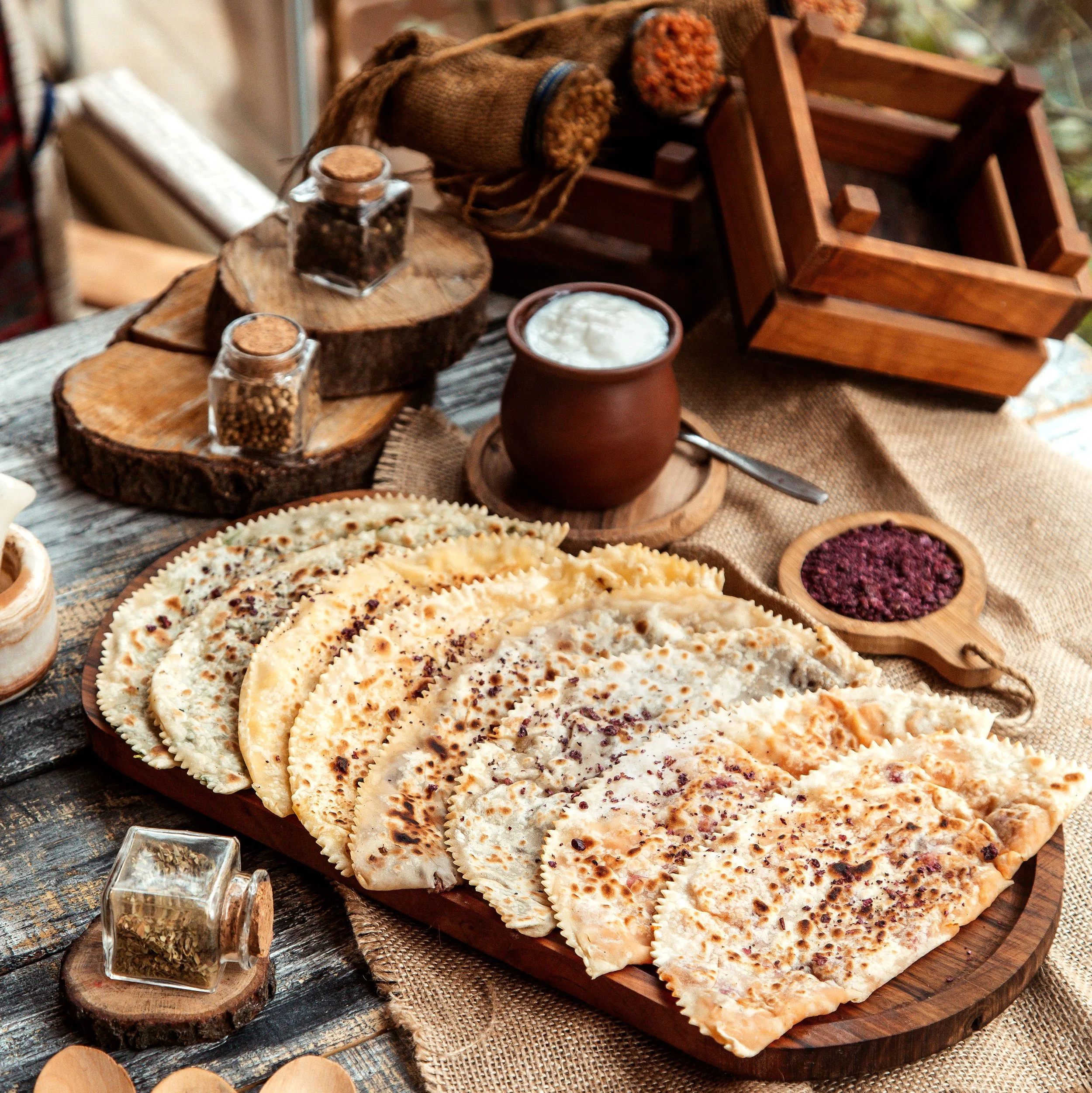 Assorted pierogis on a wooden platter surrounded by spices, sour cream, and rustic decor in a cozy setting.