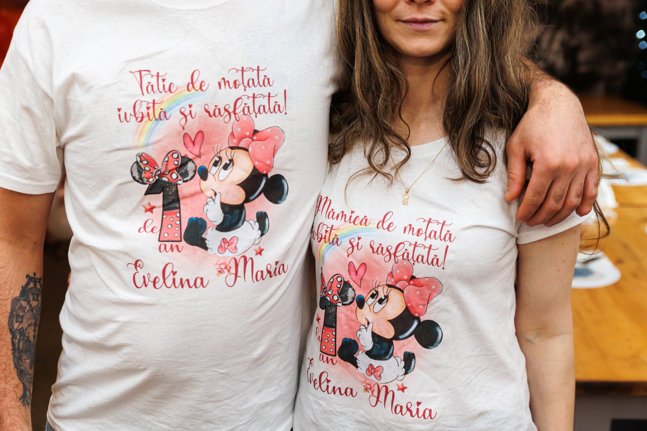 Two people wearing matching white T-shirts with colorful Minnie Mouse graphics and Romanian inscriptions, standing closely with one person's arm around the other.