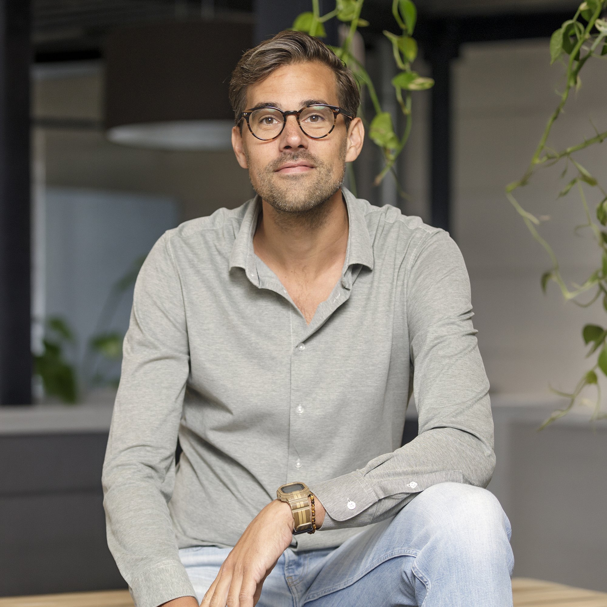 Een man met bril en een grijze polo die een polsarmband draagt, houdt iemands hand vast.