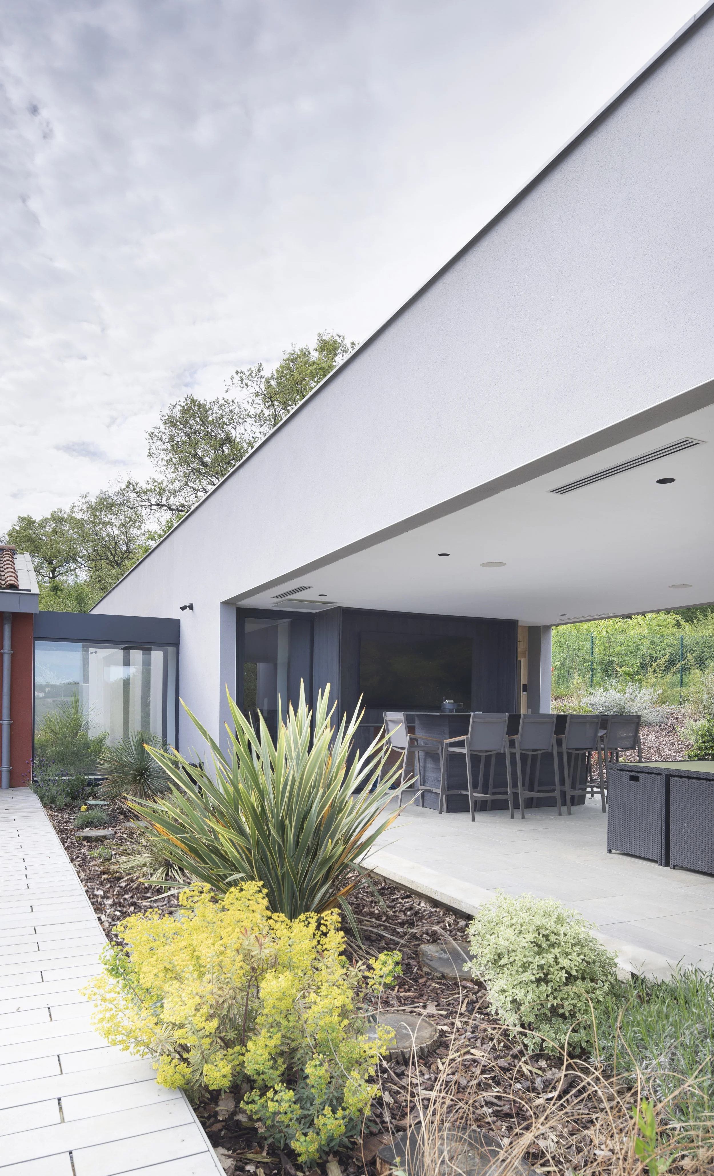 Une terrasse extérieure moderne avec un espace de repas, entourée de plantes décoratives et une maison blanche au style contemporain.