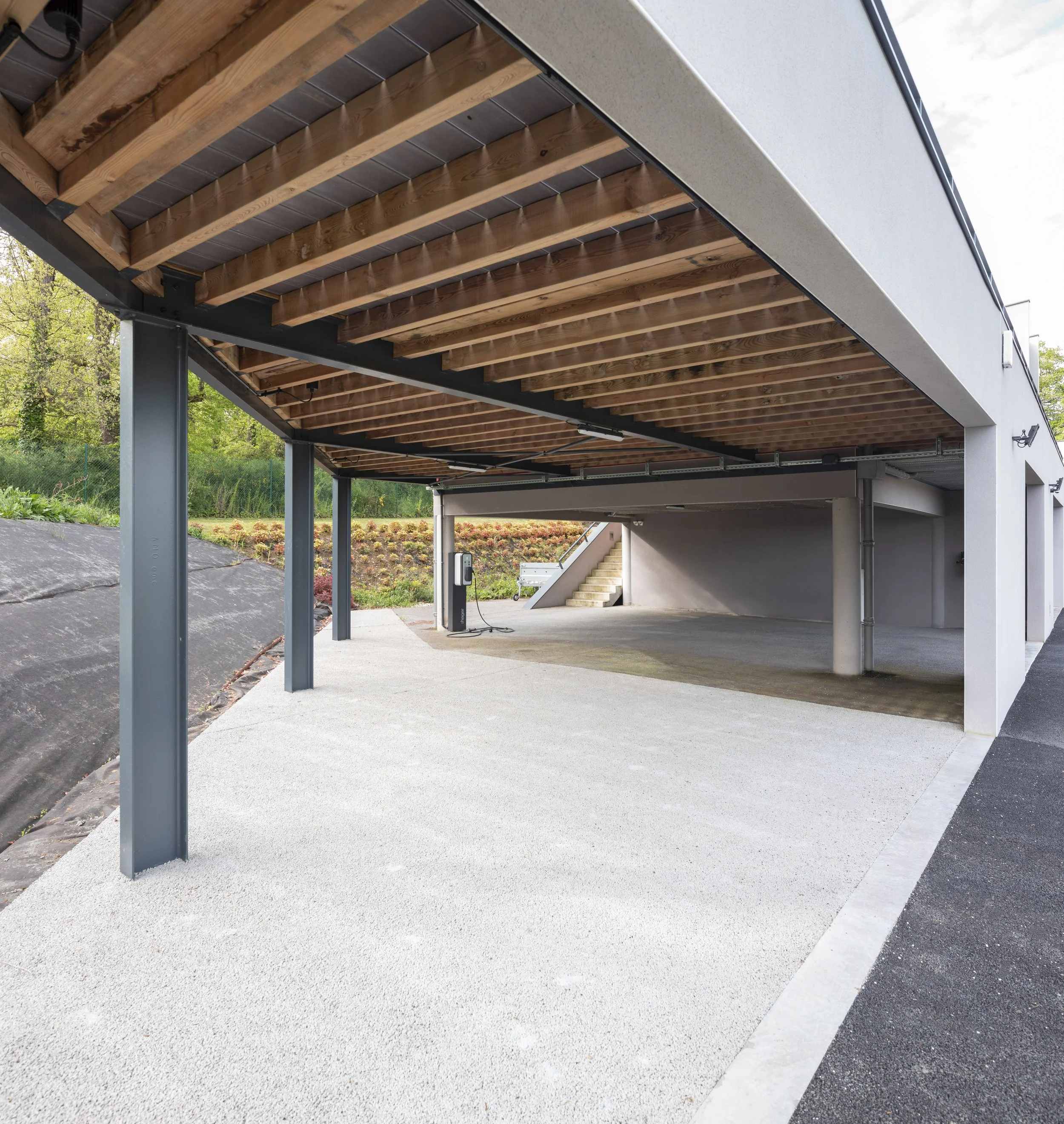 Parking sous une structure moderne avec une surface en béton et un plafond en bois.
