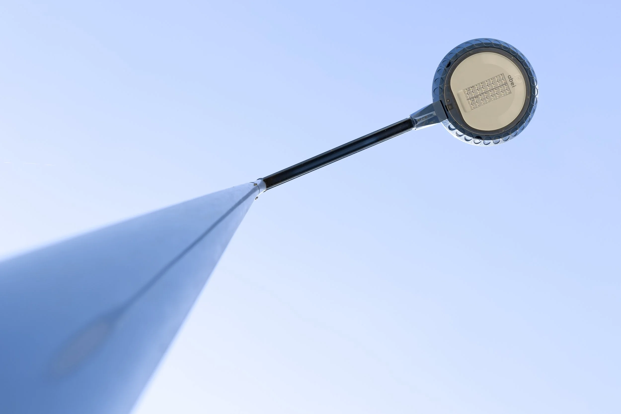 Poteau d'éclairage public vu de dessous, avec un LED rond en haut, contre un ciel clair.