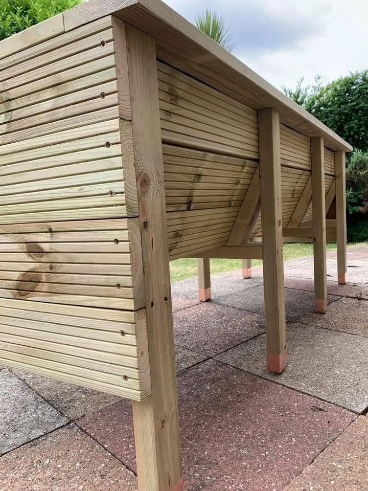 A raised wooden structure with horizontal slats and vertical support posts on a paved outdoor area.