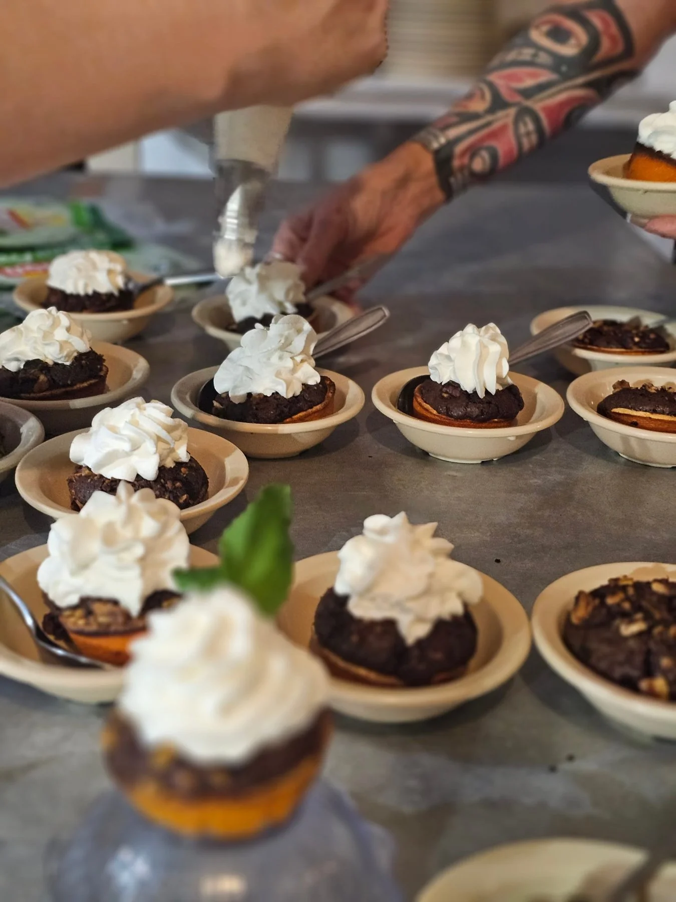 Multiple small bowls with chocolate dessert topped with whipped cream, with a person applying whipped cream on them in the background. Sara Taylor Wellness Retreat