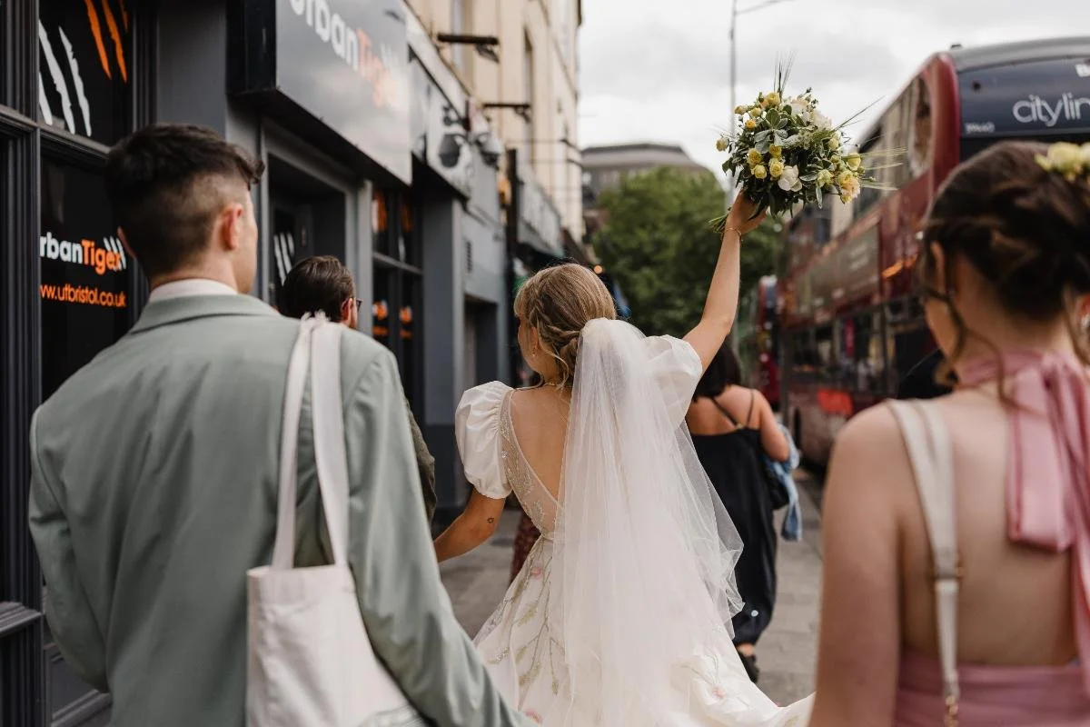 the bride walking down the street in bristol with bouquet in the air
