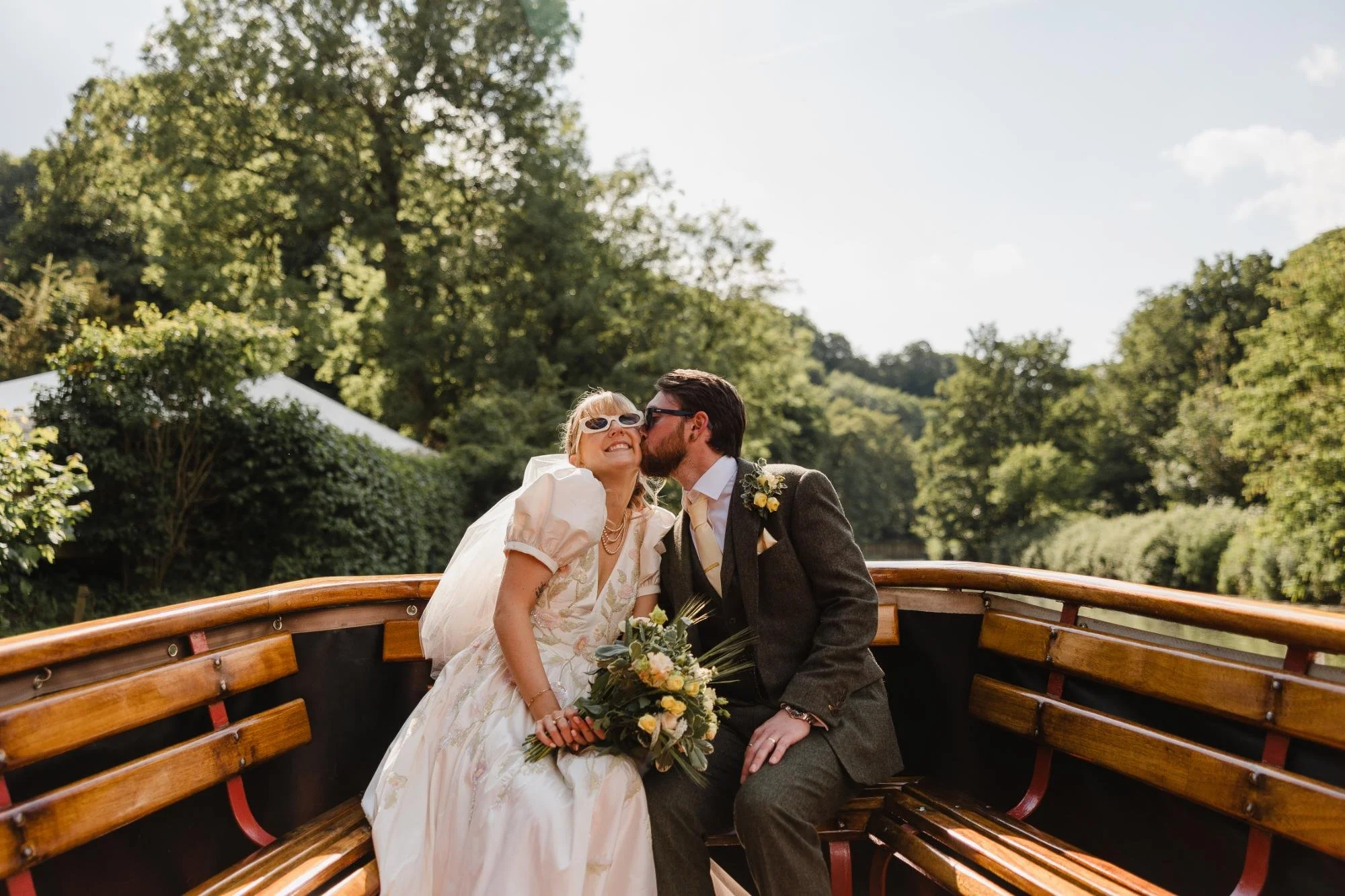 groom kissing bride on cheek both sat on boat