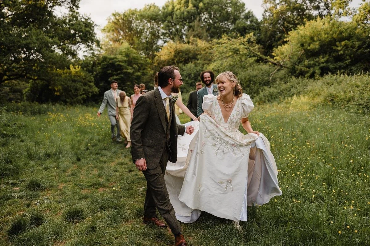 natural candid photo of bride and groom walking and laughing while wedding party walk behind