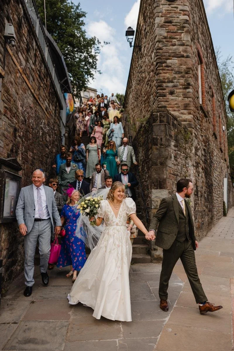 bride and groom walking through bristol with their wedding party following