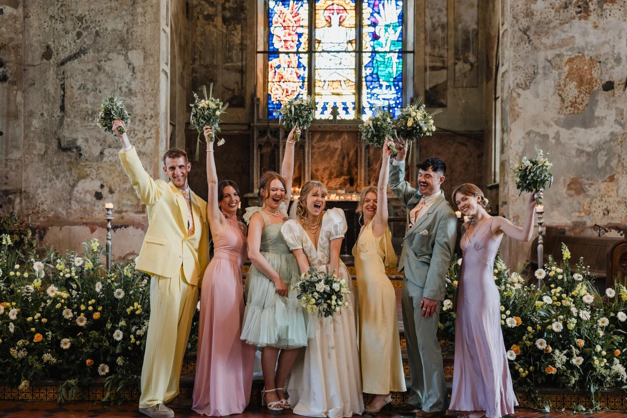 bride and bridal party in mismatched pastel outfits cheering with bouquets in air at the mount without