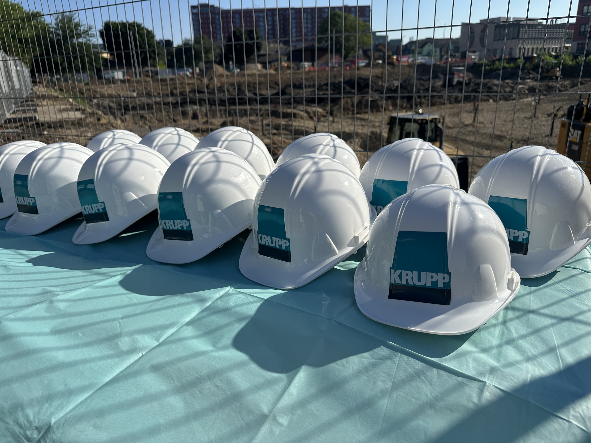 White hard hats that read "Krupp" line a table, ready for groundbreaking photos