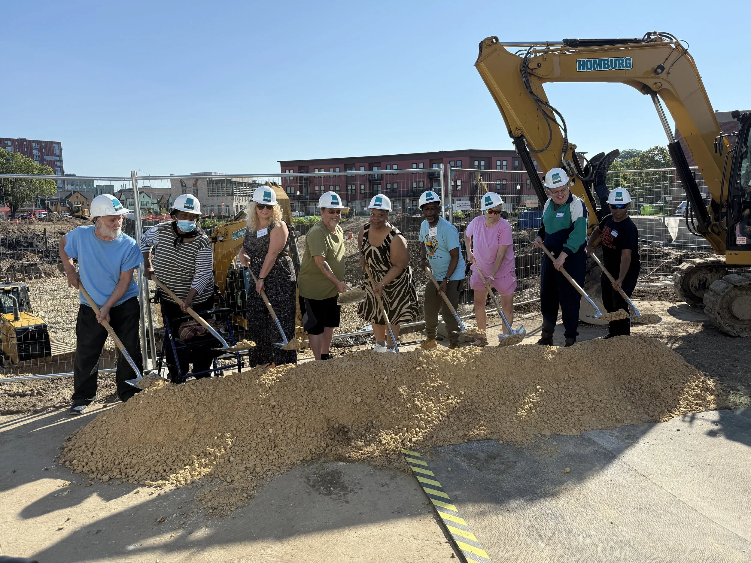 CDA Triangle residents participate in the groundbreaking photo ops. The residents hold gravel filled shovels and smile as they ceremonially break ground.
