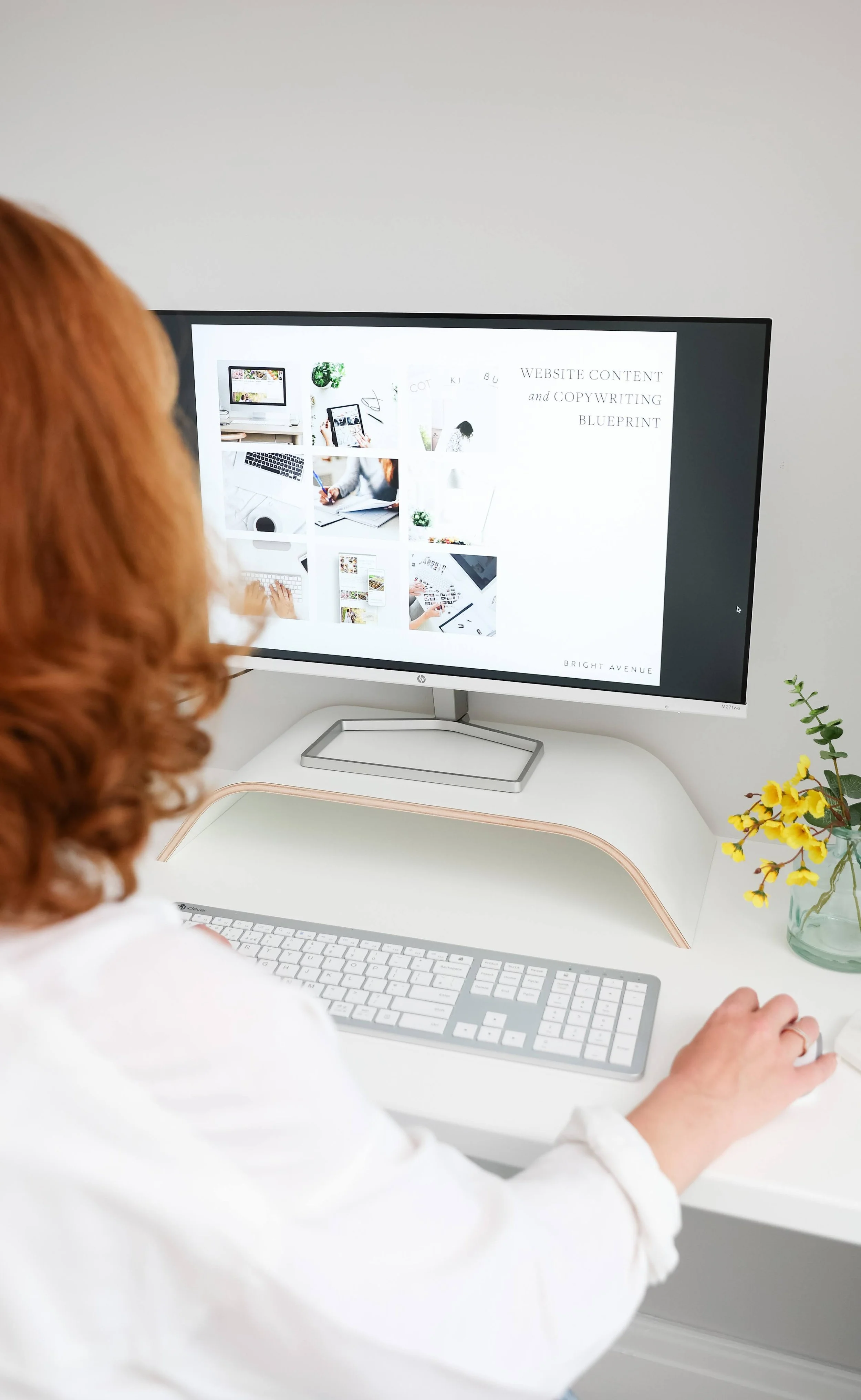 Back of red-haired web designer sitting at a white desk working on a computer