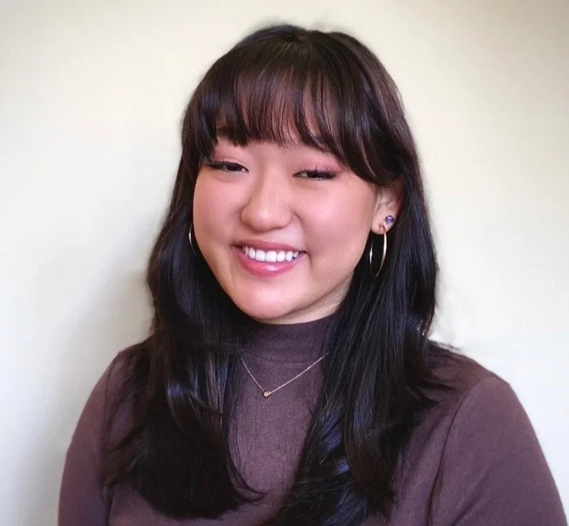 This image is a picture of Mia Kendrick from the shoulders up. She is smiling. She is a brunette and wearing a brown turtleneck top.