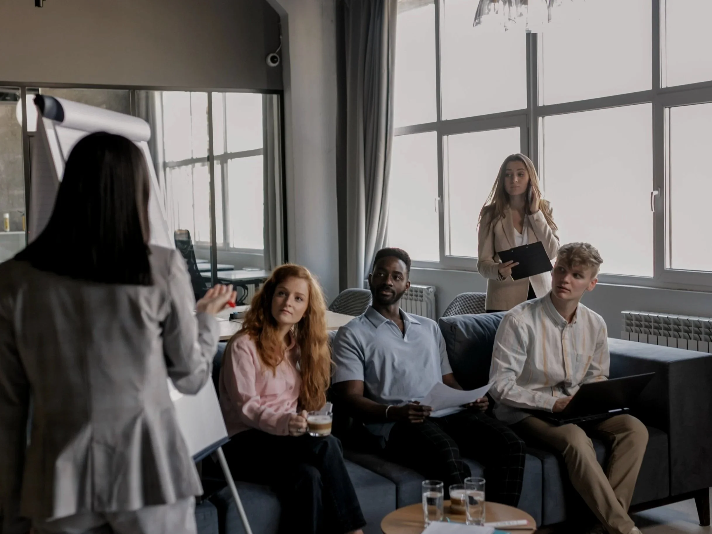 A group of young professionals are listening to a long haired colleague.