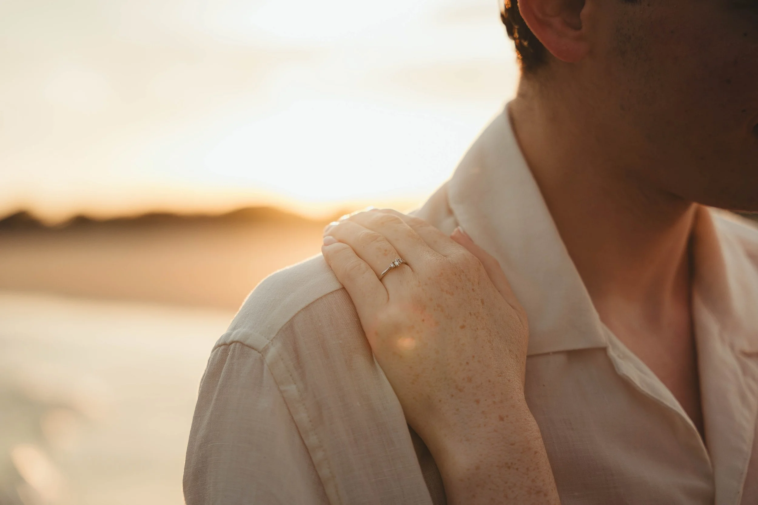 A woman touching her shoulder at sunset, wearing a ring on her finger.