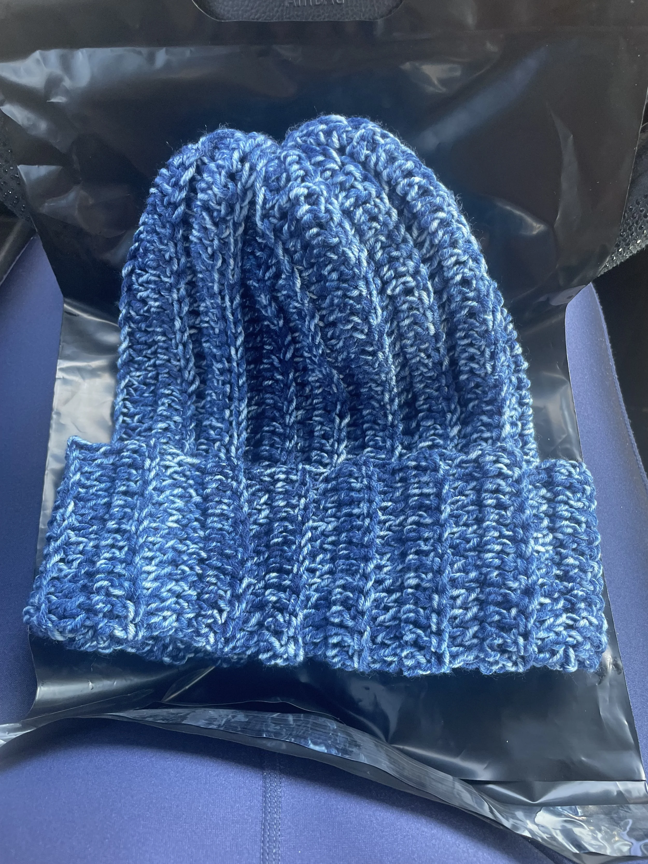 A blue knit beanie hat with a ribbed pattern, placed on a black plastic surface.