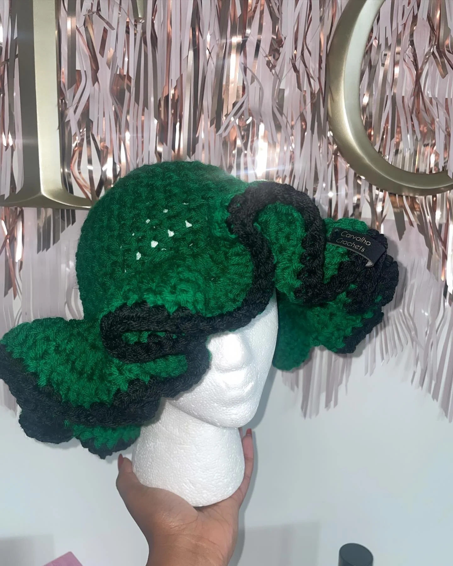 Crocheted green and black butterfly hat displayed on a white mannequin head.
